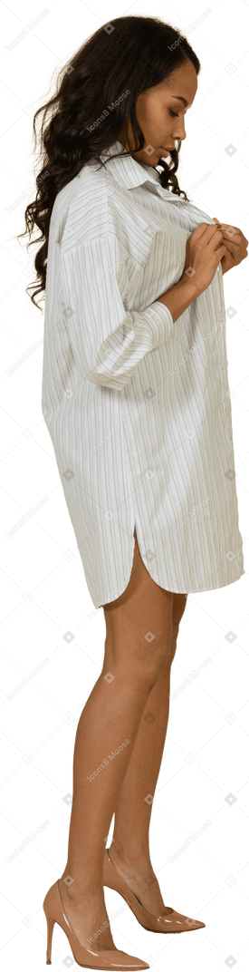 Vista laterale di una giovane femmina dalla carnagione scura che abbottona il suo vestito bianco