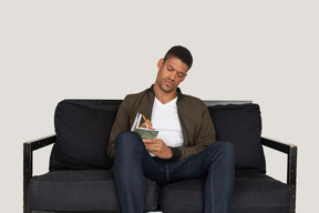 Вид спереди молодого человека, сидящего на диване и делающего заметки