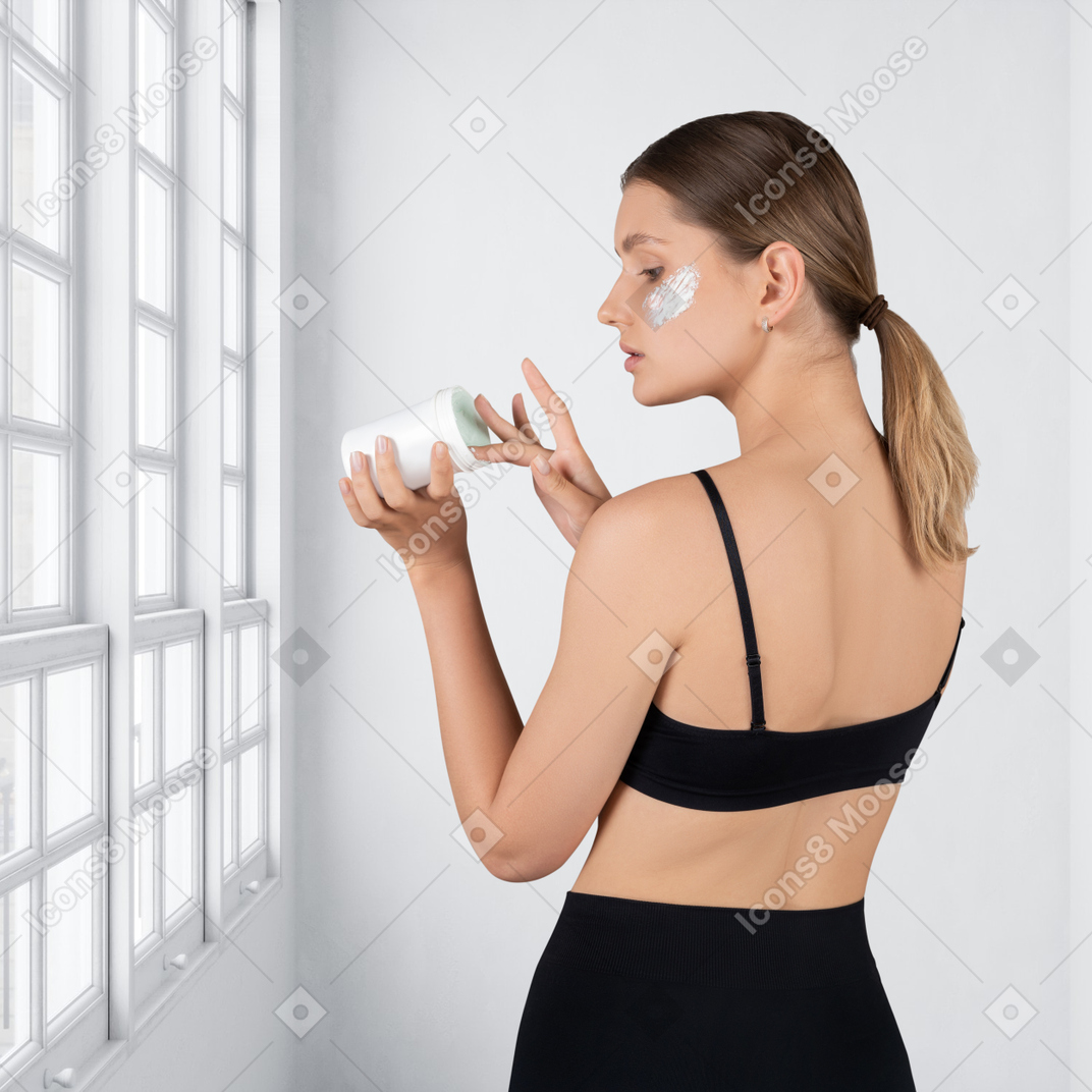 A woman in a black bra applying moisturizer