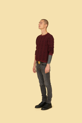 じっと立っている赤いセーターを着た若い男の4分の3のビュー