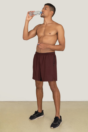 Bare chested young man in sport shorts drinking water