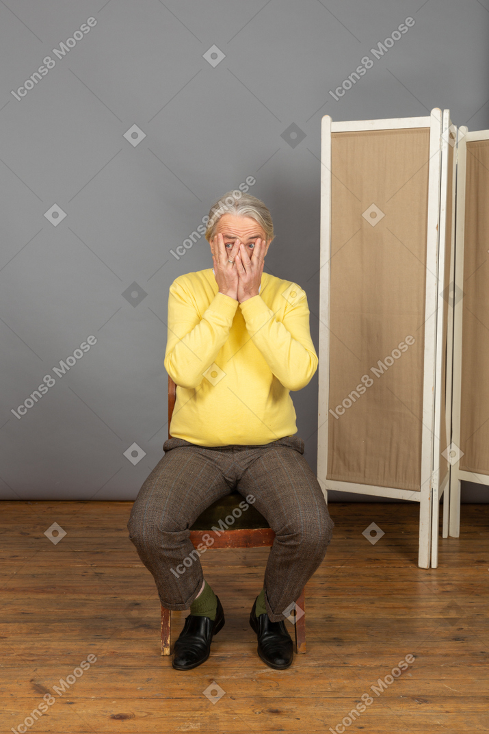 Homem de meia idade sentado na cadeira e cobrindo o rosto