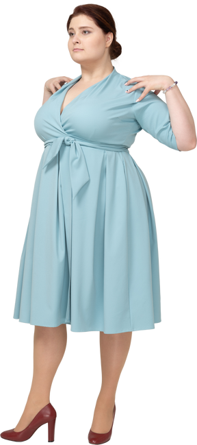 Front view of a woman in blue dress standing with hands on shoulders