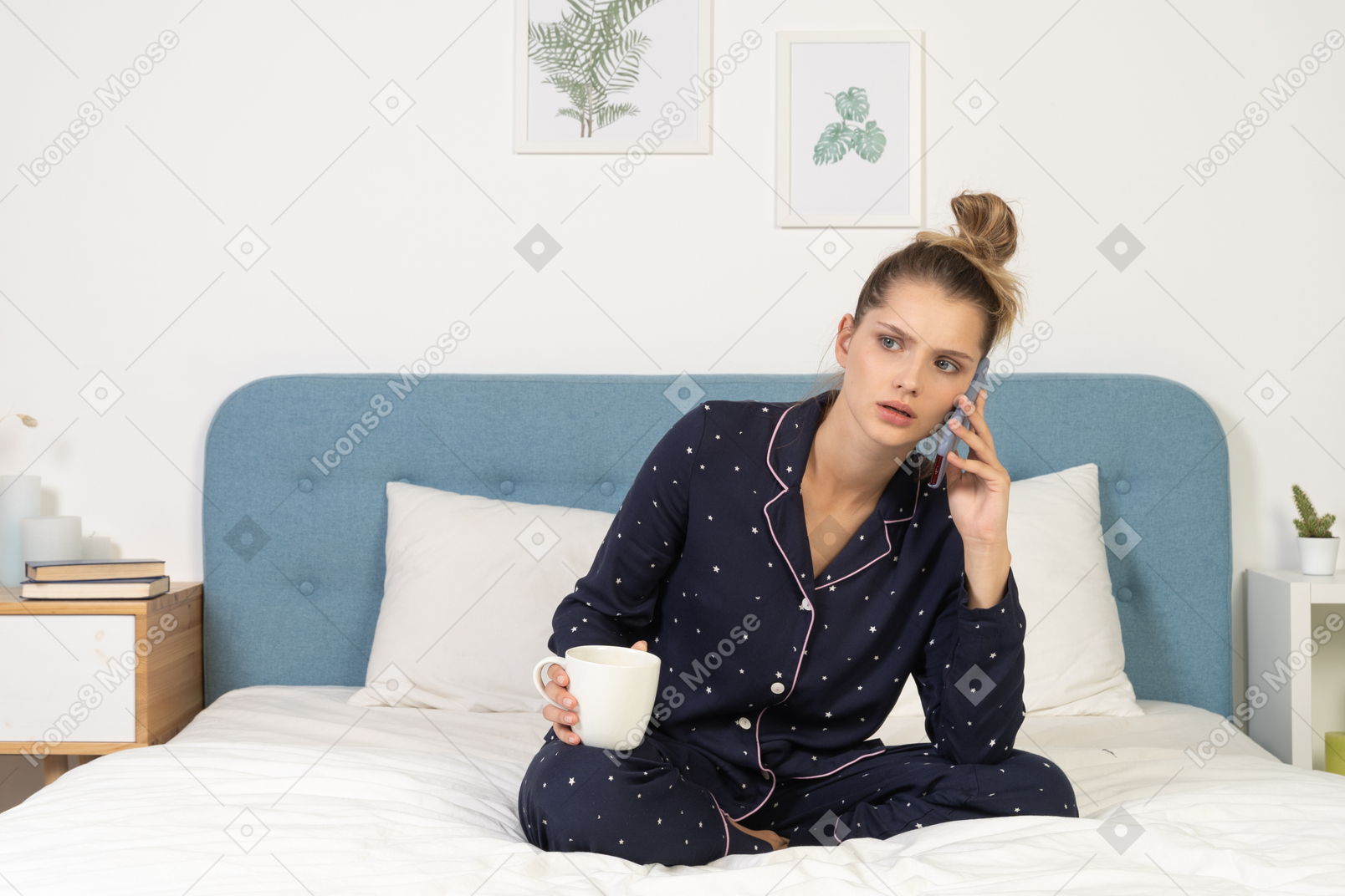 Front of a young perplexed female in pajama sitting in bed holding the cup and having a phone call