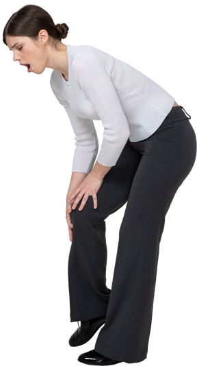 Вид сбоку молодой женщины в офисной одежде, касающейся колена