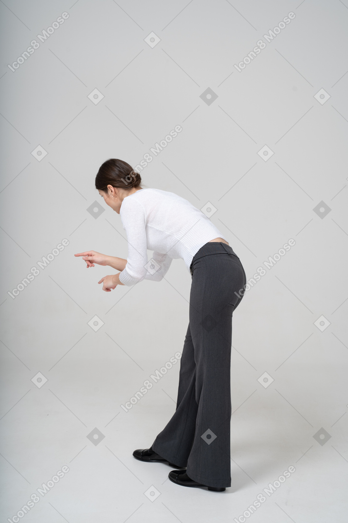 Vista lateral de uma mulher de calça preta e blusa branca se abaixando