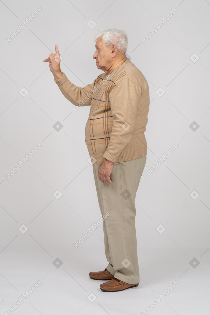 Vista lateral de um velho em roupas casuais apontando para cima com um dedo