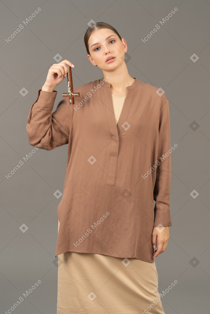 Young woman holds a christian cross upside down with her hand