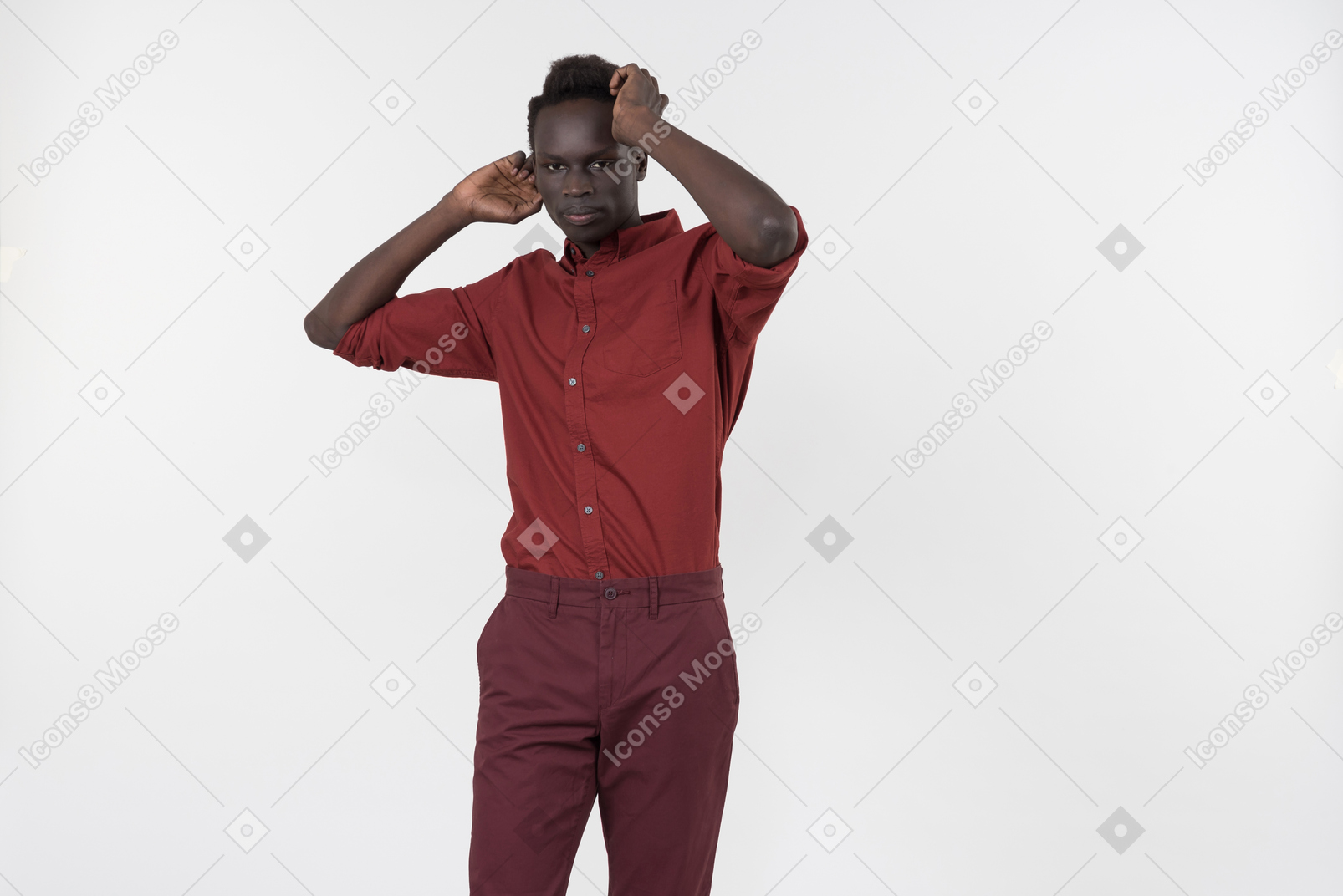 A young black man in a red shirt with rolled up sleeves and dark red pants standing alone on the white background