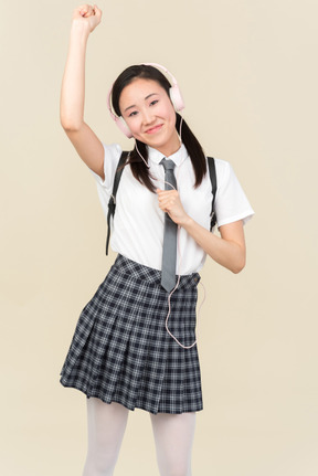 Asian school girl listening to music in headphones and dancing