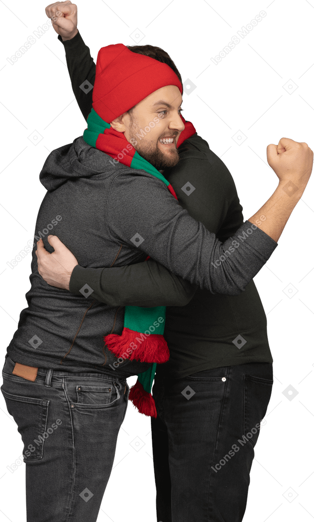 拳を握りしめている2人の感情的に抱き締める男性のサッカーファンの側面図