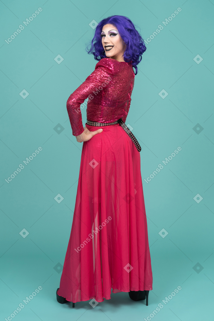 Drag queen in abito rosa sorridente e guardando sopra la spalla con le mani sui fianchi