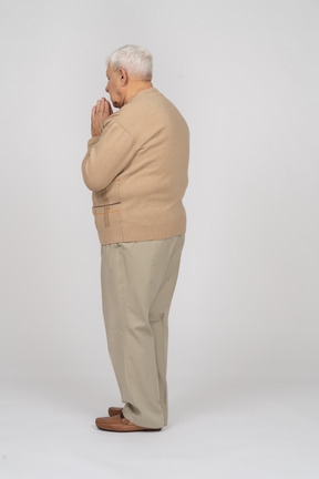 Side view of an old man in casual clothes holds hands in praying gesture