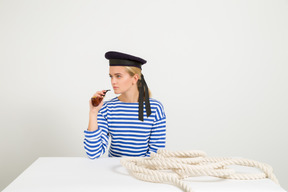 Female sailor sitting at the table woth rope on it and smoking pipe