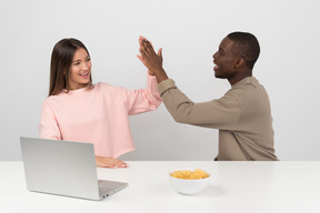 Casal atraente fazendo high five enquanto assistia a algum show on-line