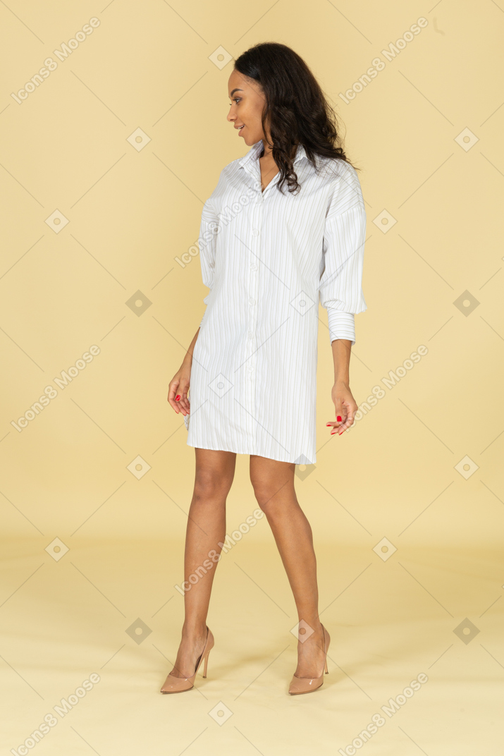 Vue de trois quarts d'une jeune femme souriante à la peau sombre en robe blanche