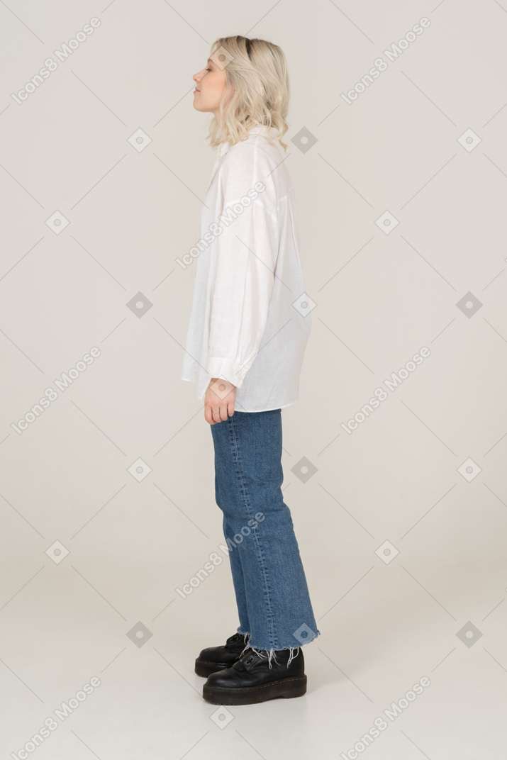 Side view of a blonde female in casual clothes standing still with her eyes closed