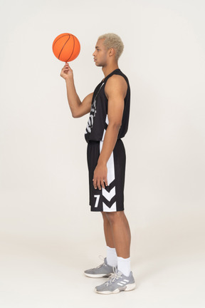 Vista posterior de tres cuartos de un joven jugador de baloncesto masculino sosteniendo una pelota