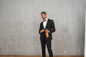 Мужчина в костюме и галстуке-бабочке стоит с бутылкой в руке