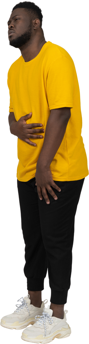 Three-quarter view of a young dark-skinned man in yellow t-shirt touching stomach