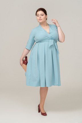 Vista frontal de uma mulher de vestido azul posando com a mão no ombro