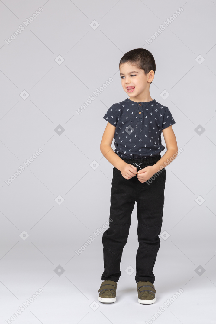 一个穿着休闲服的可爱男孩的前视图，看着一边，露出舌头
