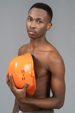 A shirtless young man holding a safety helmet