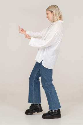 Side view of a blonde female stepping forward and showing middle finger on both hands