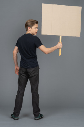 Ernsthafter junger mann, der mit einem leeren plakat steht