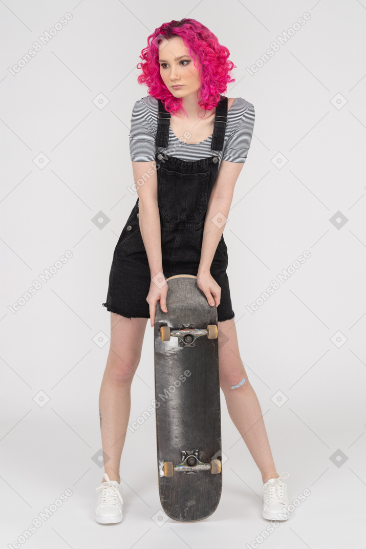 Uma menina de cabelos rosa, apoiando-se em um skate