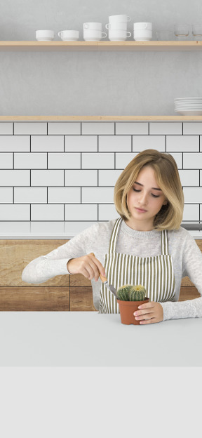 A woman in an apron caring for a pot plant in a kitchen