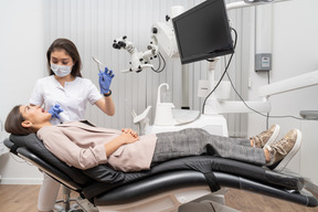 Comprimento total de uma dentista segurando um instrumento odontológico e uma paciente em um armário de hospital