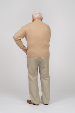 腰に手を置いて立っているカジュアルな服装の老人の背面図