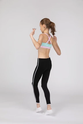 Vista posterior de tres cuartos de una jovencita en ropa deportiva caminando cautelosamente de puntillas