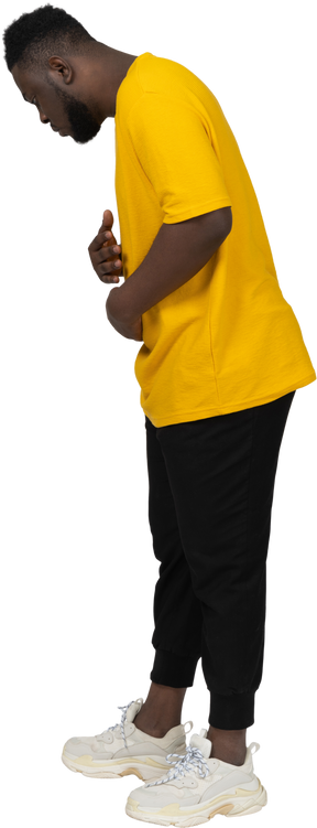 Side view of a young dark-skinned man in yellow t-shirt touching stomach & looking down