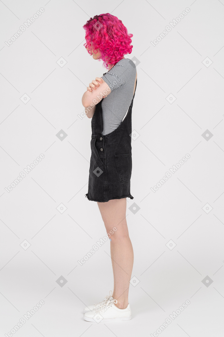 Pink haired girl standing in profile with her arms folded