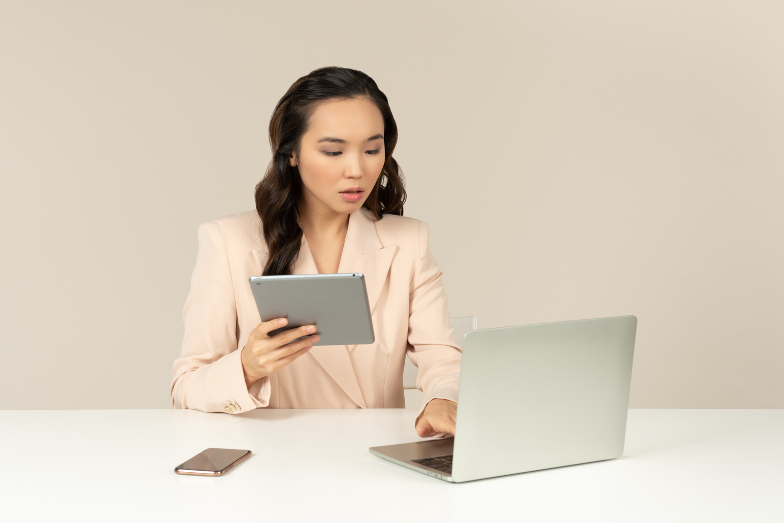 Asian female office employee working on laptop and holding tablet