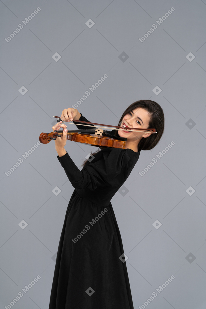 Primo piano di una giovane donna allegra in abito nero a suonare il violino