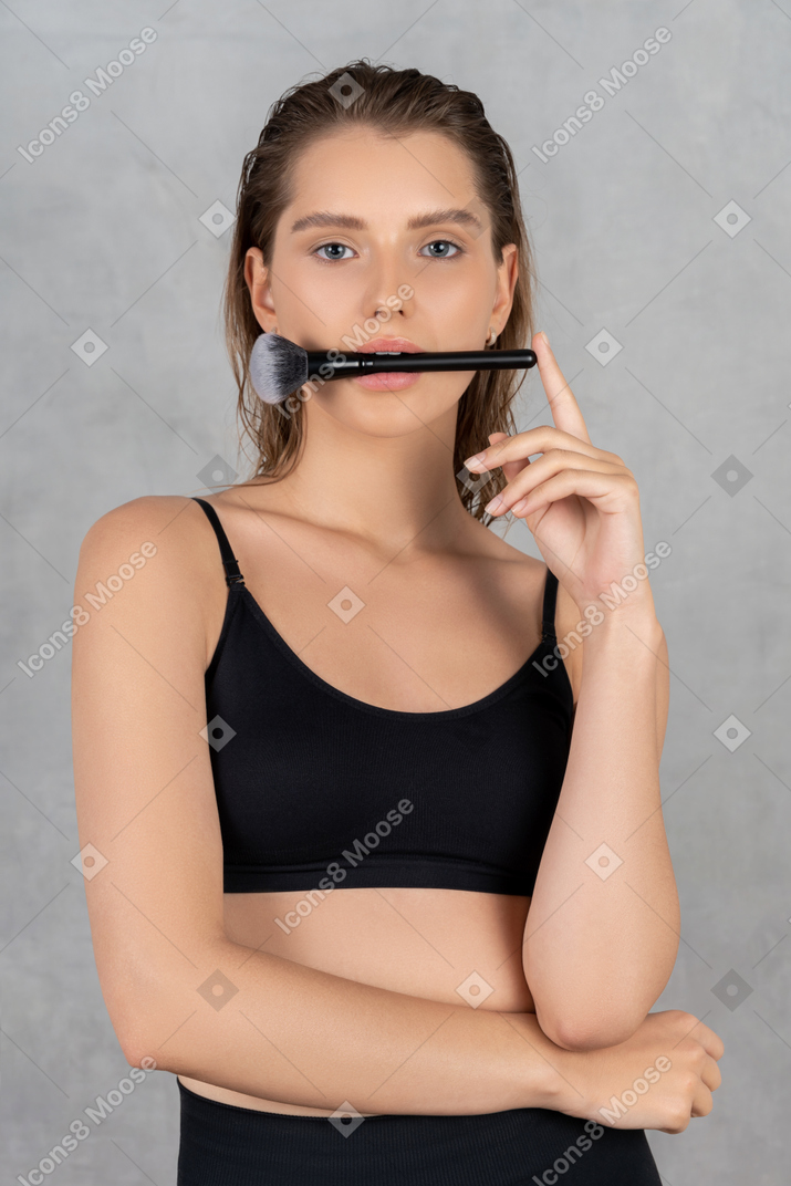 Красивая женщина держит кисточку для макияжа во рту