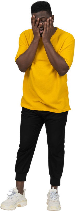 Vorderansicht eines erschöpften jungen dunkelhäutigen mannes in gelbem t-shirt, der sein gesicht berührt