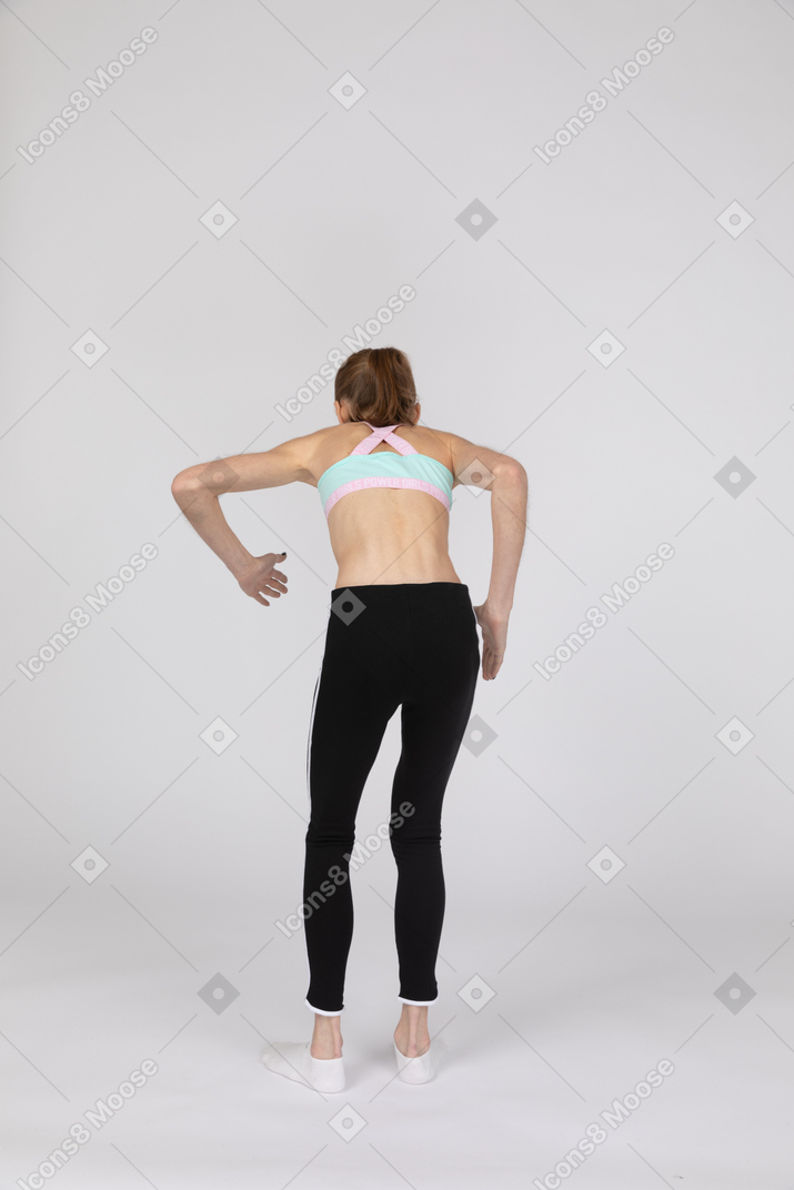 Vista traseira de uma adolescente em roupas esportivas inclinando-se para a frente em pé como um robô