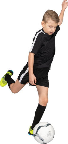 Трехчетвертный вид мальчика в футбольной форме, бьющего по мячу