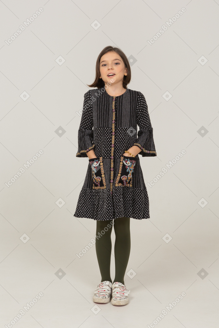 Vue de face d'une petite fille souriante en robe mettant les mains dans les poches