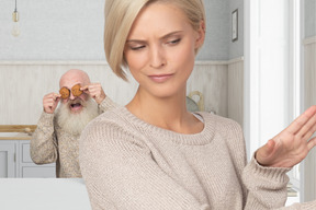 Aged man closing eyes with cookies and young woman irritated with his behaviour