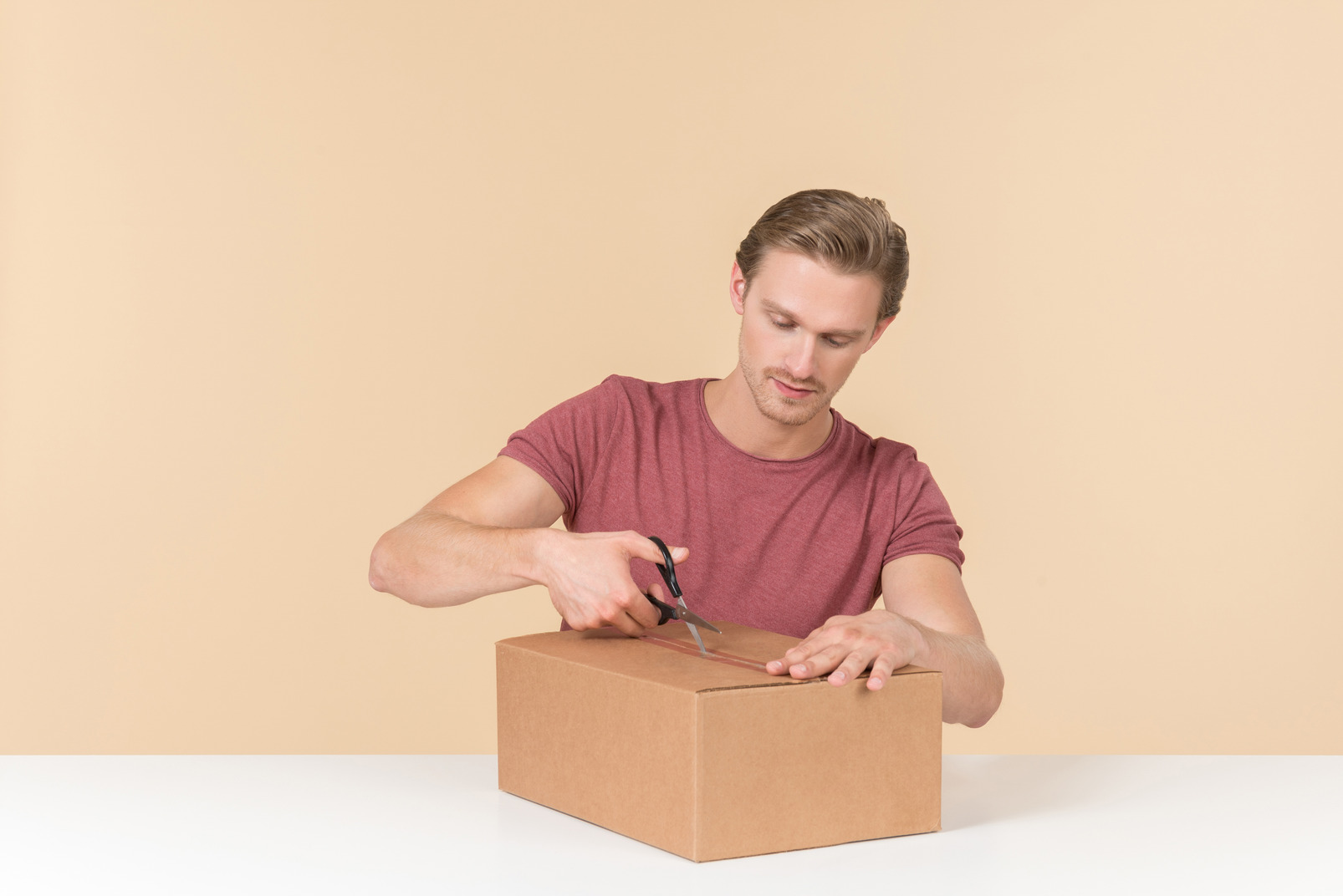 Young guy opening a parcel with scissors