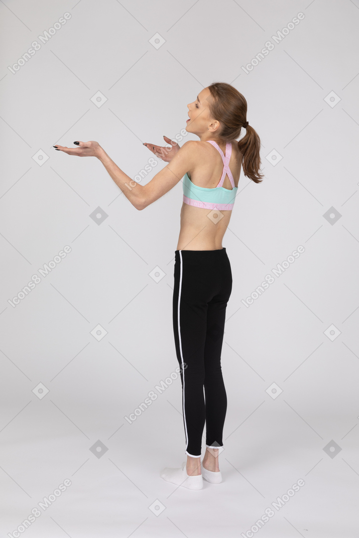 Vista traseira de uma adolescente surpresa em roupas esportivas, levantando as mãos e abrindo a boca