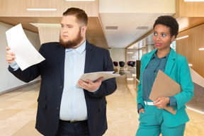 A man looking at papers standing next to a woman holding clipboard