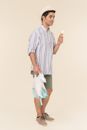 Young caucasian guy holding avoska and eating ice cream