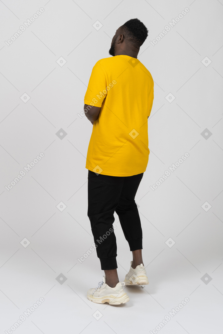 Vista posteriore di tre quarti di un giovane uomo dalla pelle scura in maglietta gialla