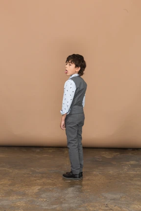 Side view of a boy in grey suit showing tongue